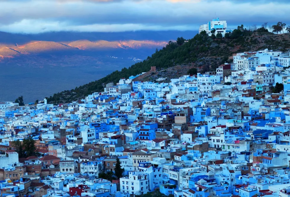 Aerial view of the blue-painted buildings of Chefchaouen against the Rif Mountains.
